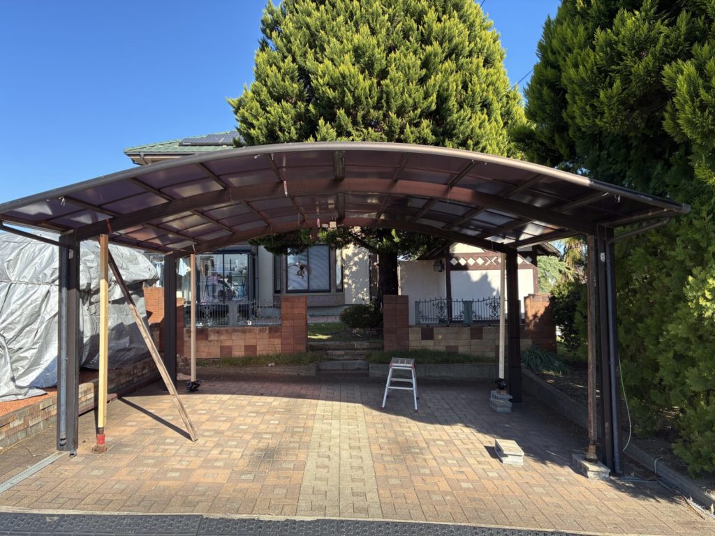 昭和アルミのカーポートの高さ調整DIYで20cmアップ途中でジャッキが伸びきったので真ん中に支柱を入れてジャッキの下にブロックを入れ高さ再調整をするところ(手前)